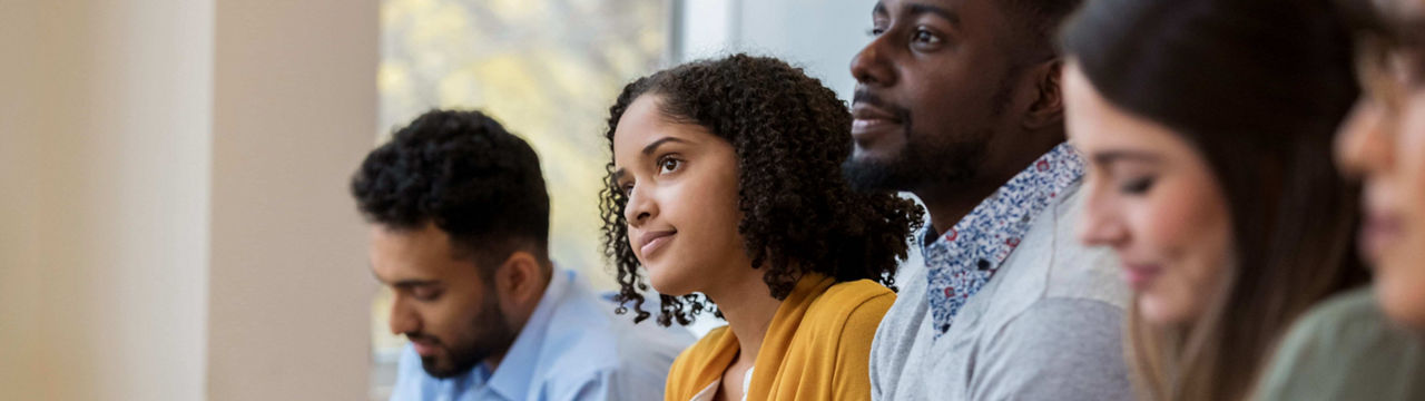 A group of business people sit in a row in a training class. They look at an unseen speaker as they concentrate on the lecture.