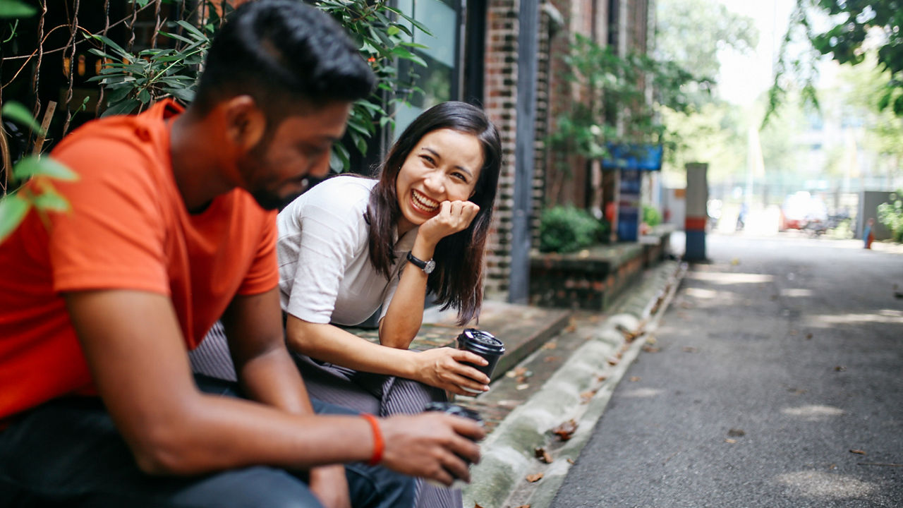 Young people talking and flirting on the streets of Kuala Lumpur, having a coffee break together in front of their office or university library.