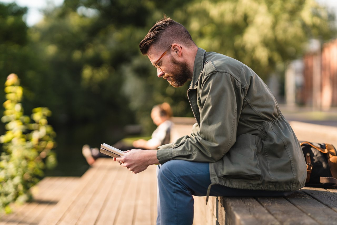 Man reading a paperback book in a public park
