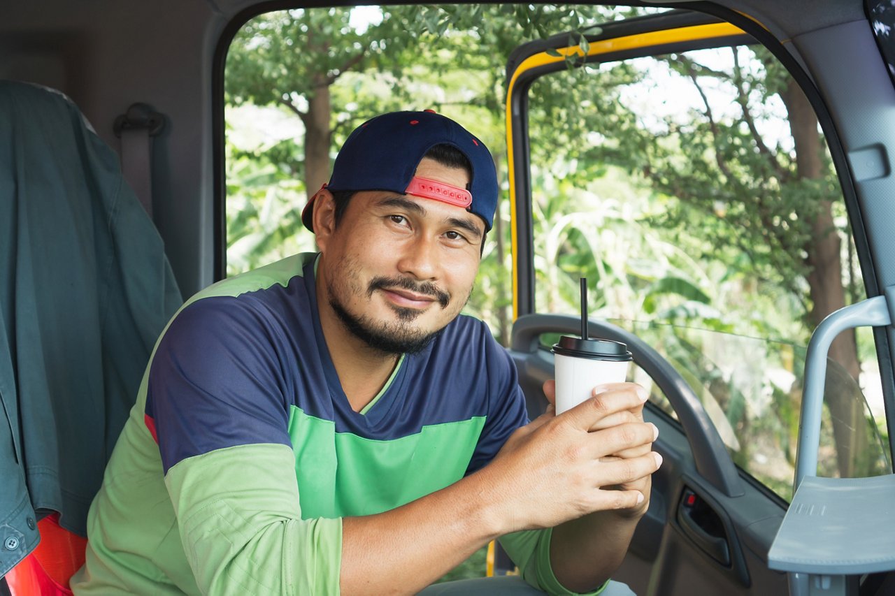 Smile Confidence positive optimistic Young Man Professional Truck Driver In Business Long transport. worker male relax holds coffee mug drink in parking lot. owner Transportation delivery semi-truck