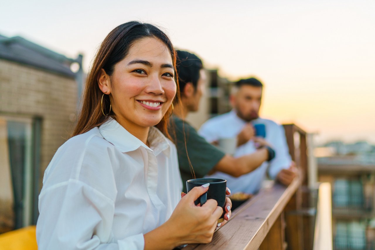 A portrait of a young woman looking at the camera during social gathering with friends at the balcony